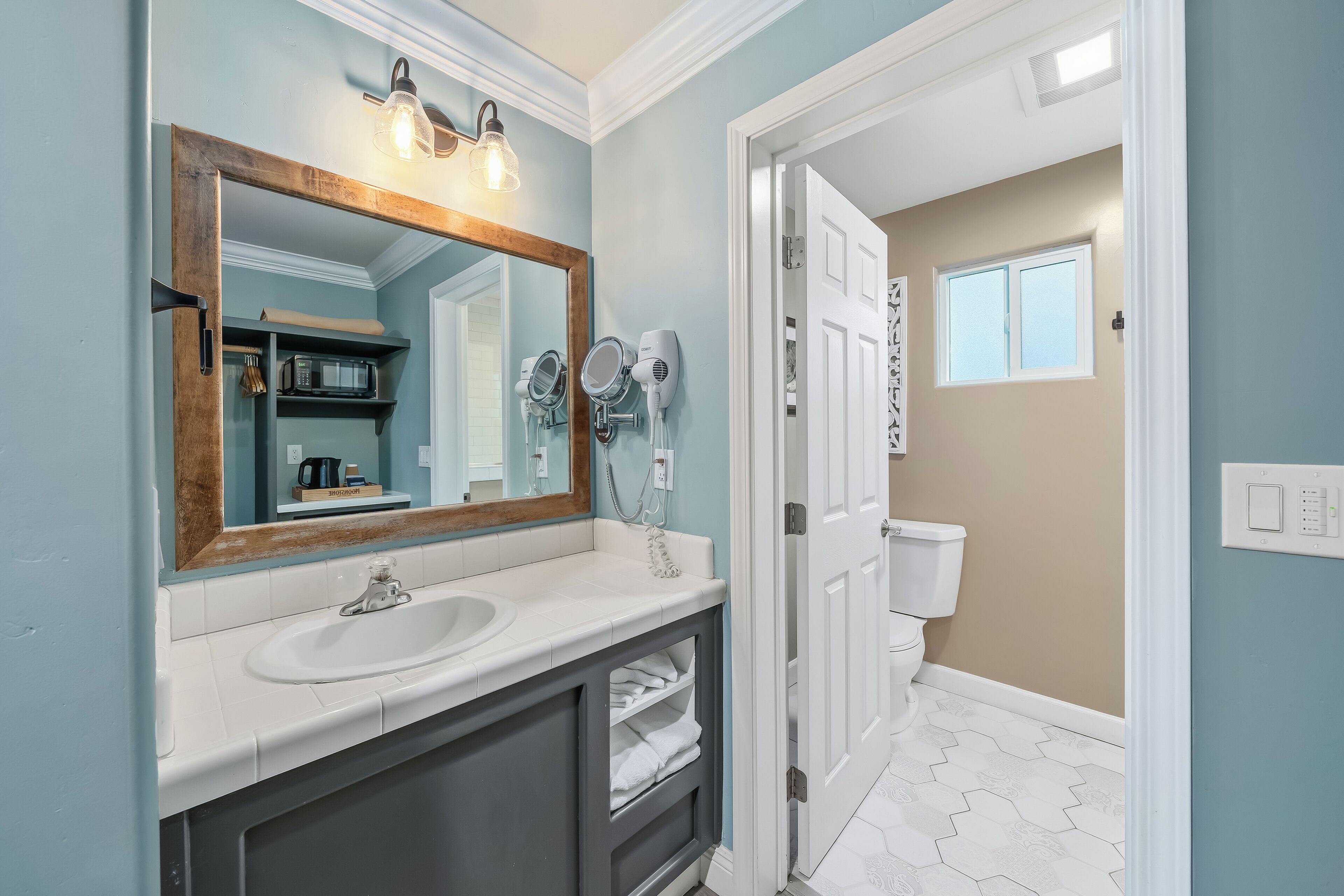 A bathroom with a large mirror, white sink, and hair dryers.