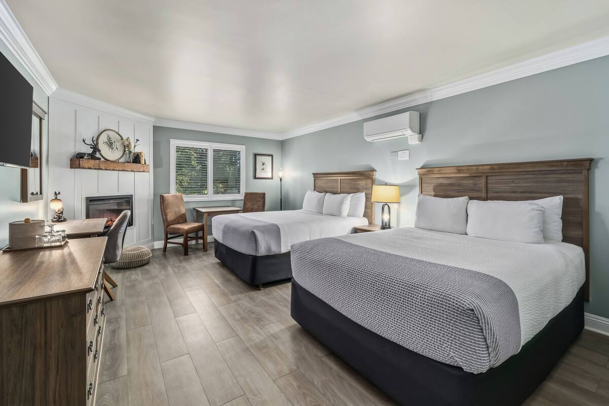 A hotel room with two beds, a desk, a chair, a fireplace, and a window.