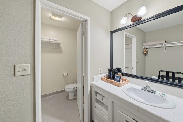 Un baño con un lavamanos blanco, un espejo y un inodoro visible en la habitación contigua.