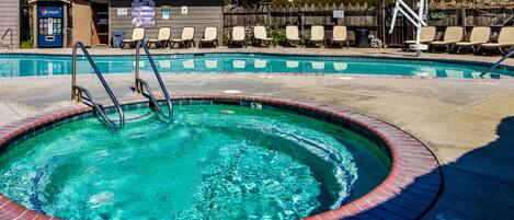 A swimming pool with a hot tub, lounge chairs, and a Pepsi vending machine.