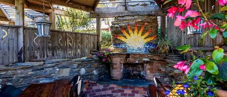 A rustic outdoor patio with a brick fire pit, wooden furniture, and a decorative sun mosaic.