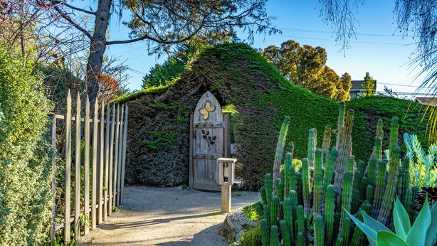 A garden with a wooden gate, a cactus, and a wooden structure with a door. - Cambria Pines Lodge (Cambria)