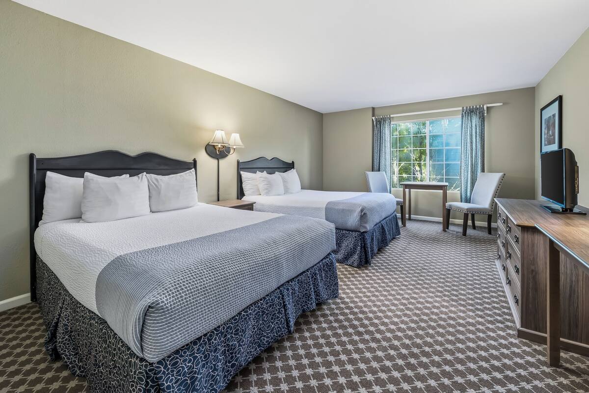 A hotel room with two beds, a desk with a chair, a TV, and a window with curtains.
