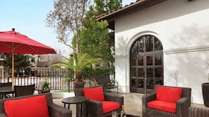 An outdoor patio area with wicker furniture, red cushions, and a potted plant. - Hilton Garden Inn Cupertino (Cupertino)