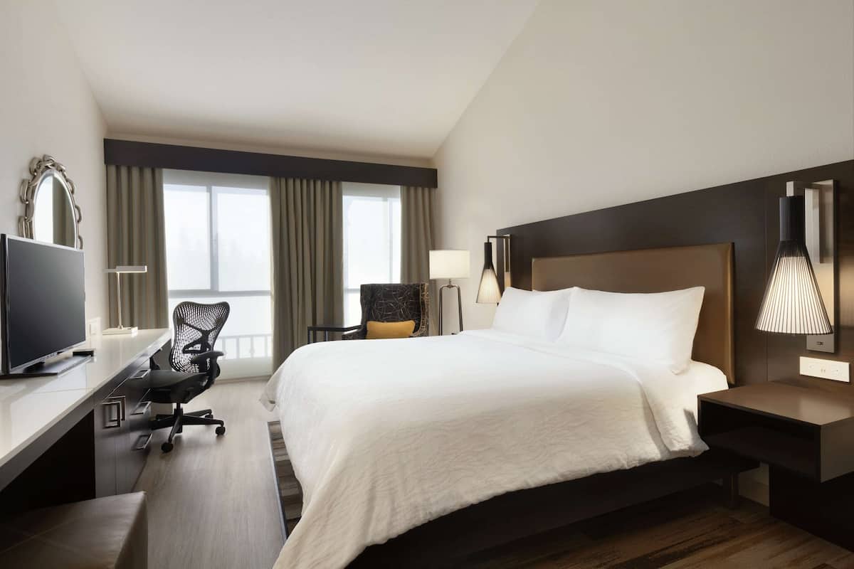 A hotel room with a large bed, a desk with a computer, a chair, and a TV.