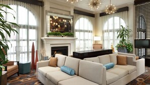 A modern living room with a fireplace, two sofas, a TV, and large windows with sheer curtains. - Hilton Garden Inn Cupertino (Cupertino)