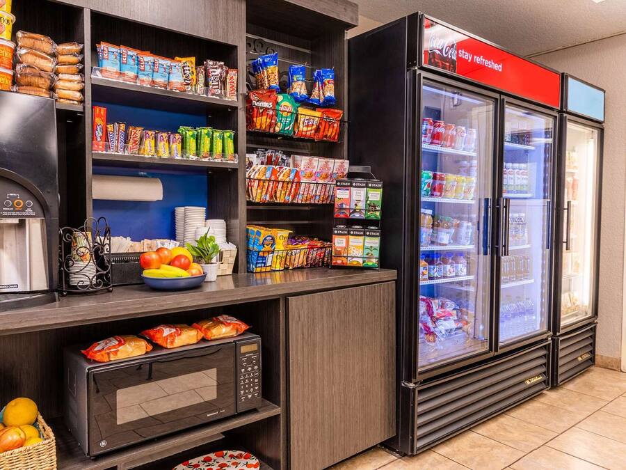 Uma estação de autoatendimento com máquina de café, micro-ondas e geladeira abastecida com lanches e bebidas.