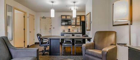 A modern hotel room with a dining area, a kitchen, and a seating area with leather chairs.