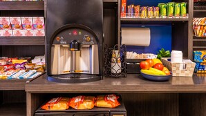 A self-serve coffee station with a coffee machine, snacks, and a bowl of fruit.