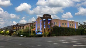 A hotel with a prominent 'Travelodge' sign, a parking lot, and a clear sky with clouds.