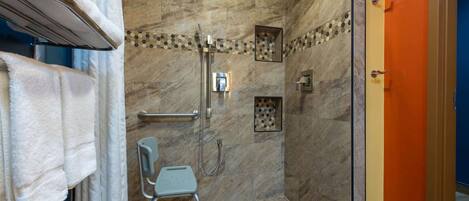 A shower area with a handrail, a showerhead, a small step stool, and a tiled floor.