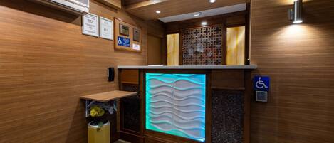 A modern restroom with wooden paneling, a wall-mounted air conditioner, a decorative light panel, and a disabled access sign.