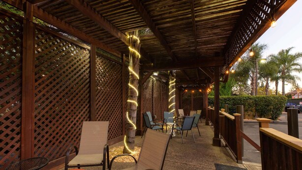 An outdoor seating area with wooden lattice walls, chairs, and tables, featuring string lights.