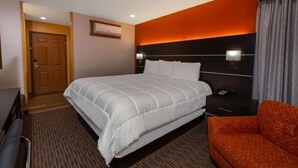 A hotel room with a large bed, a bedside table with a lamp, a red sofa, and a wooden door.