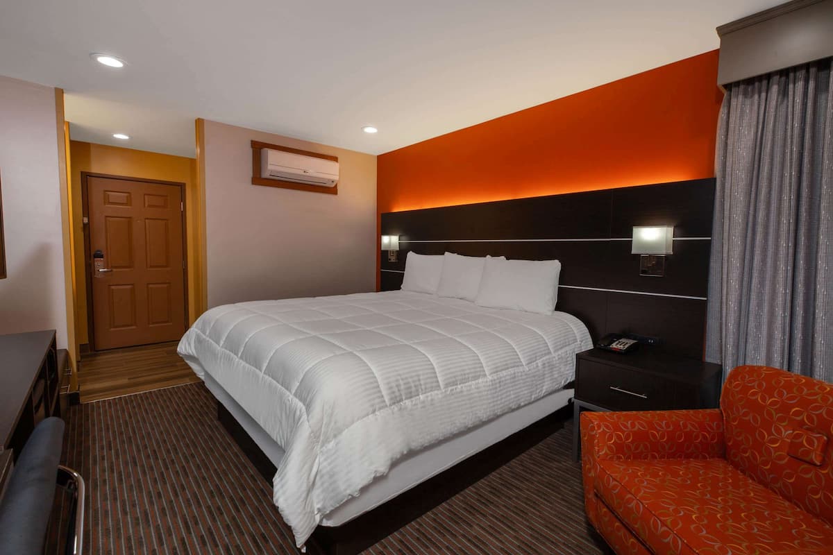 Una habitación de hotel con una cama grande, una mesita de noche con una lámpara, un sofá rojo y una puerta de madera.