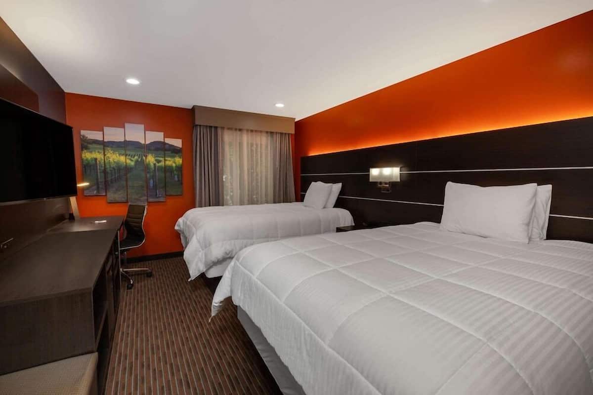 Habitación de hotel con dos camas, un escritorio, un televisor y un cuadro en la pared.
