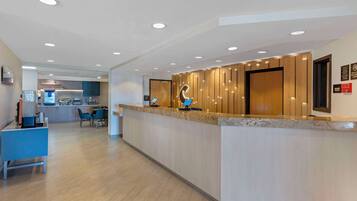A modern hotel reception area with a counter, seating, and a visible kitchenette in the background.
