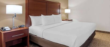 A hotel room with a large bed, wooden headboard, two bedside tables with lamps, a telephone, and a small drawer.