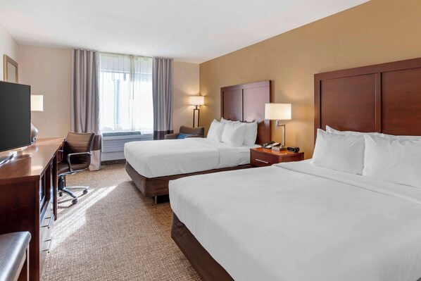 A hotel room with two beds, a desk, a chair, a TV, and a window with curtains.