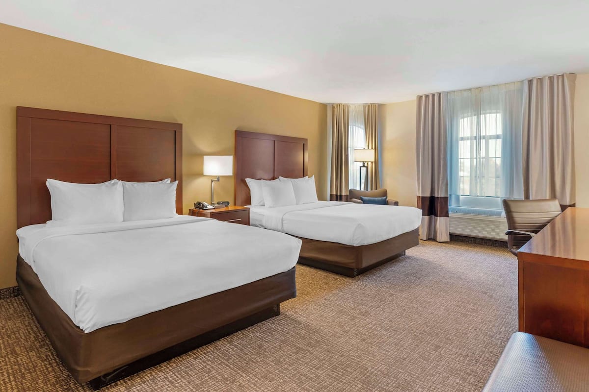 Een hotelkamer met twee bedden, een bureau, een stoel, een lamp en een raam met gordijnen.