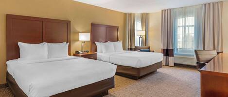 A hotel room with two beds, a desk, a chair, a lamp, and a window with curtains.