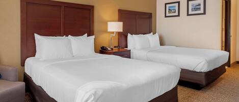 A hotel room with two beds, a nightstand, a lamp, and two framed pictures on the wall.