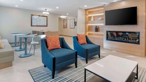 A modern hotel lobby with seating areas, a flat-screen TV, and a fireplace.