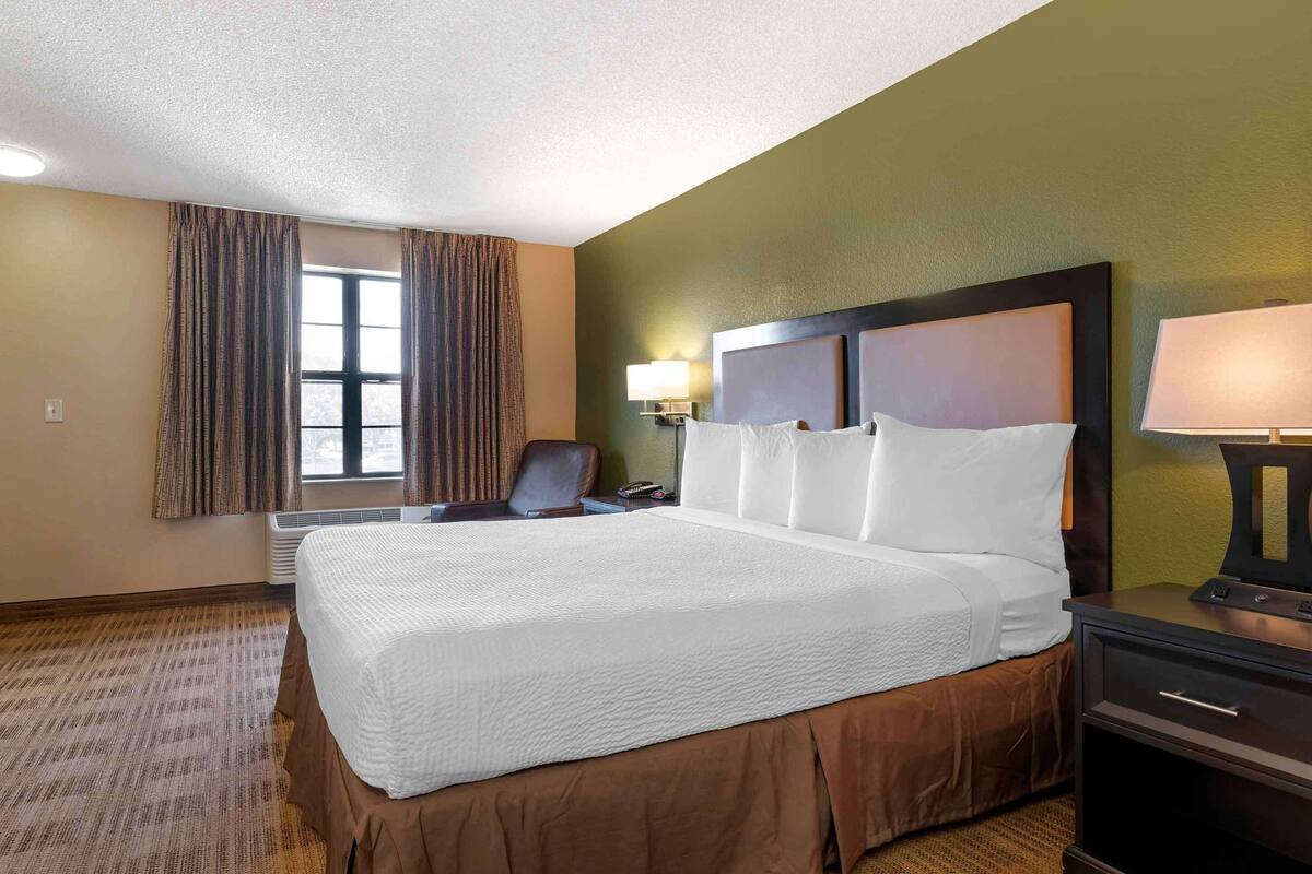 Une chambre d’hôtel avec un grand lit, un bureau, une chaise, une lampe et une fenêtre avec des rideaux.