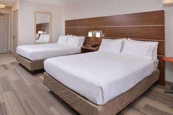 A hotel room with two beds, a wooden headboard, bedside tables with lamps, and a carpeted floor.