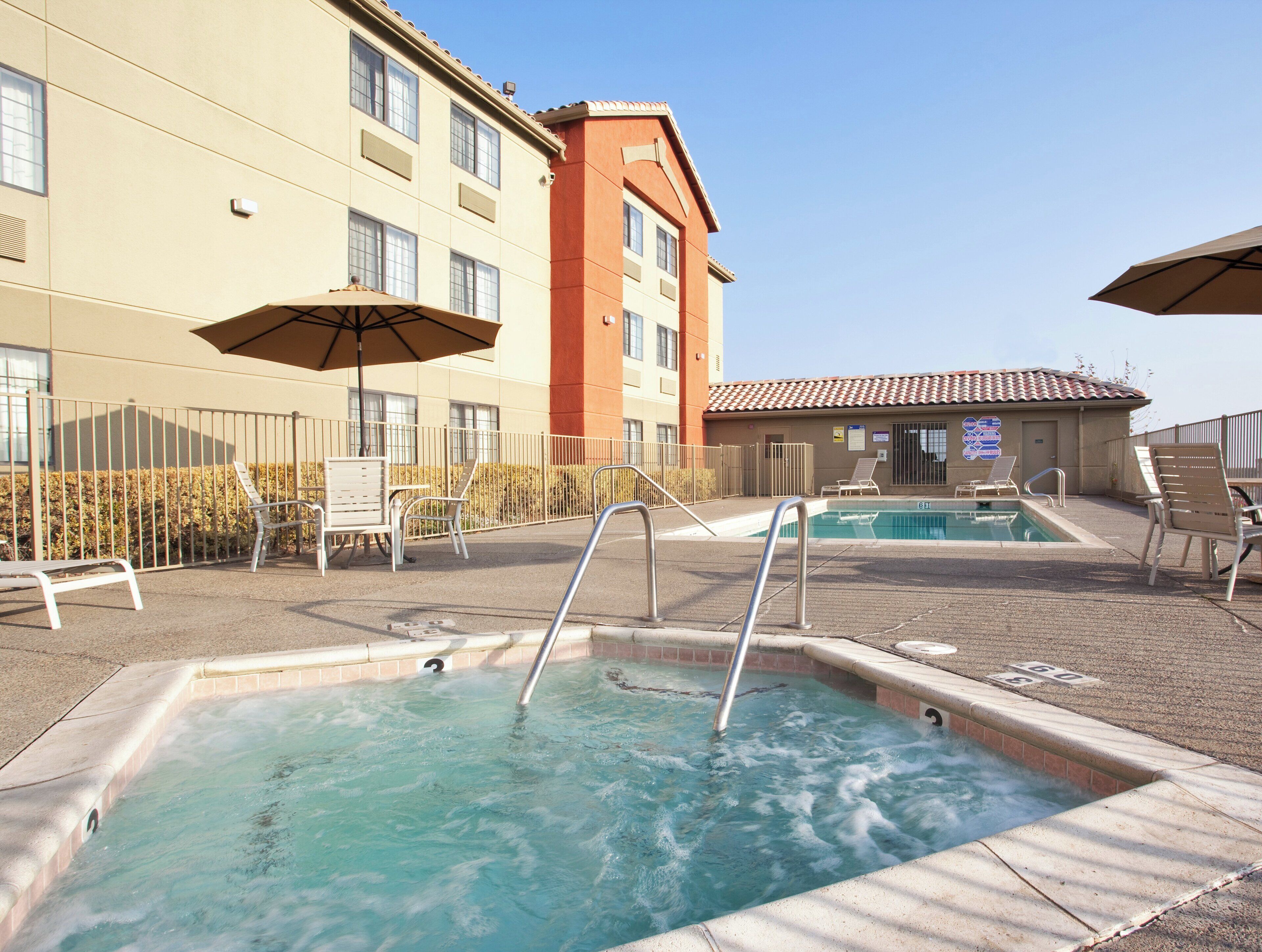 Een zwembadgedeelte van een hotel met twee whirlpools, ligbedden en parasols.