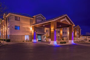 A hotel entrance with a covered driveway, a gated driveway, and a building facade with illuminated windows.