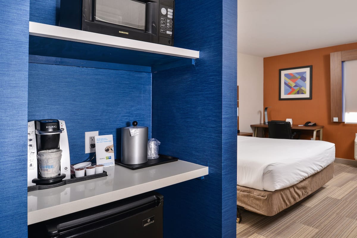 Ein Hotelzimmer mit Küchenzeile, einschließlich Mikrowelle, Kaffeemaschine und kleinem Kühlschrank. Ein Bett und ein Schreibtisch mit Stuhl sind vorhanden.