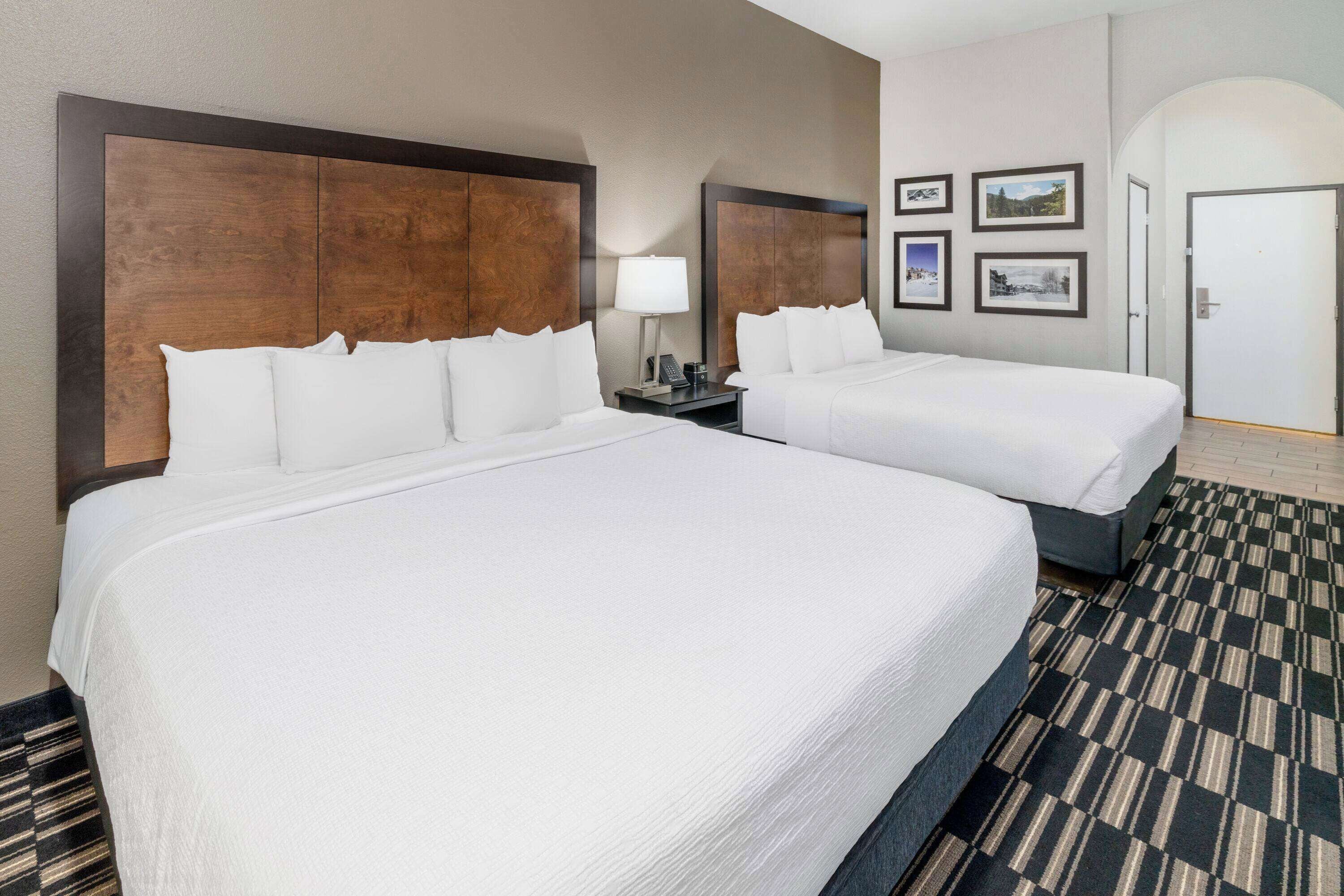 A hotel room with two beds, a nightstand with a lamp, and framed pictures on the wall.