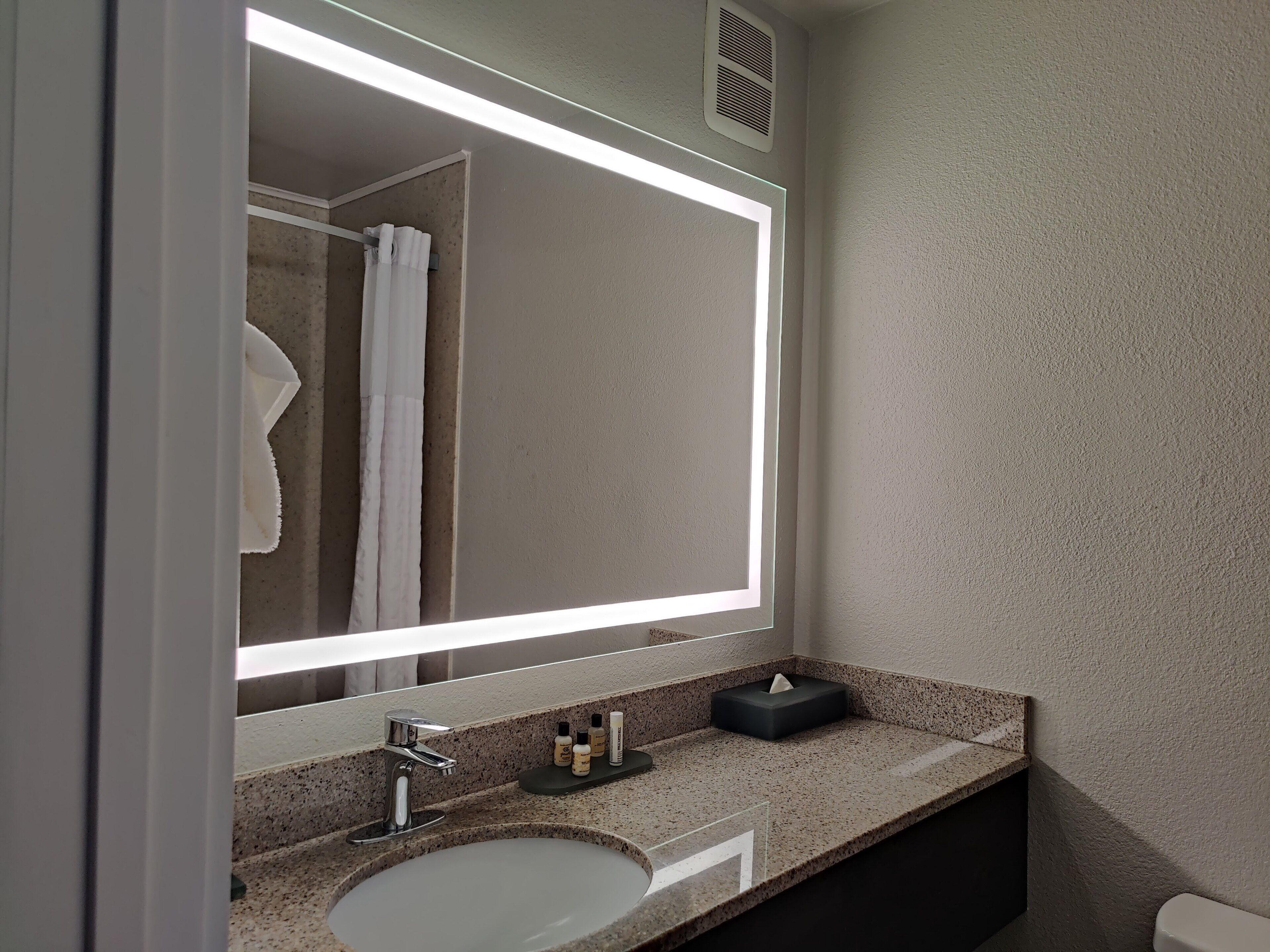 A bathroom with a large mirror, a sink, and a towel rack.