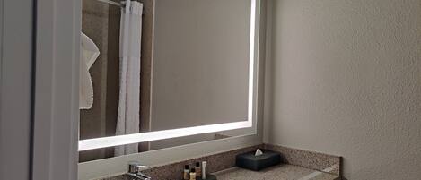 Un baño con un espejo grande, un lavamanos y un perchero para toallas.