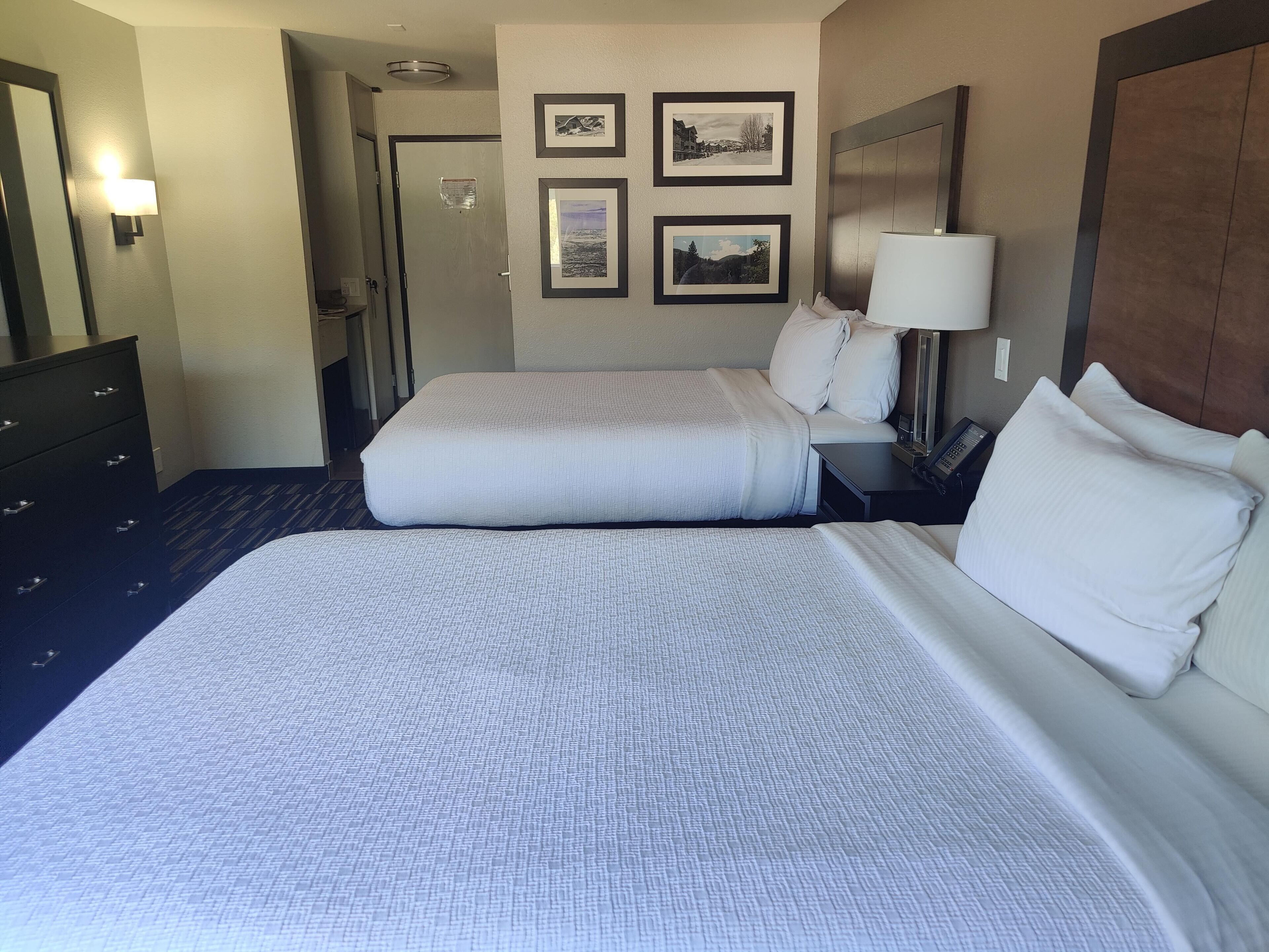 Une chambre d’hôtel avec deux lits, une commode, une table de chevet avec une lampe et des tableaux encadrés au mur.