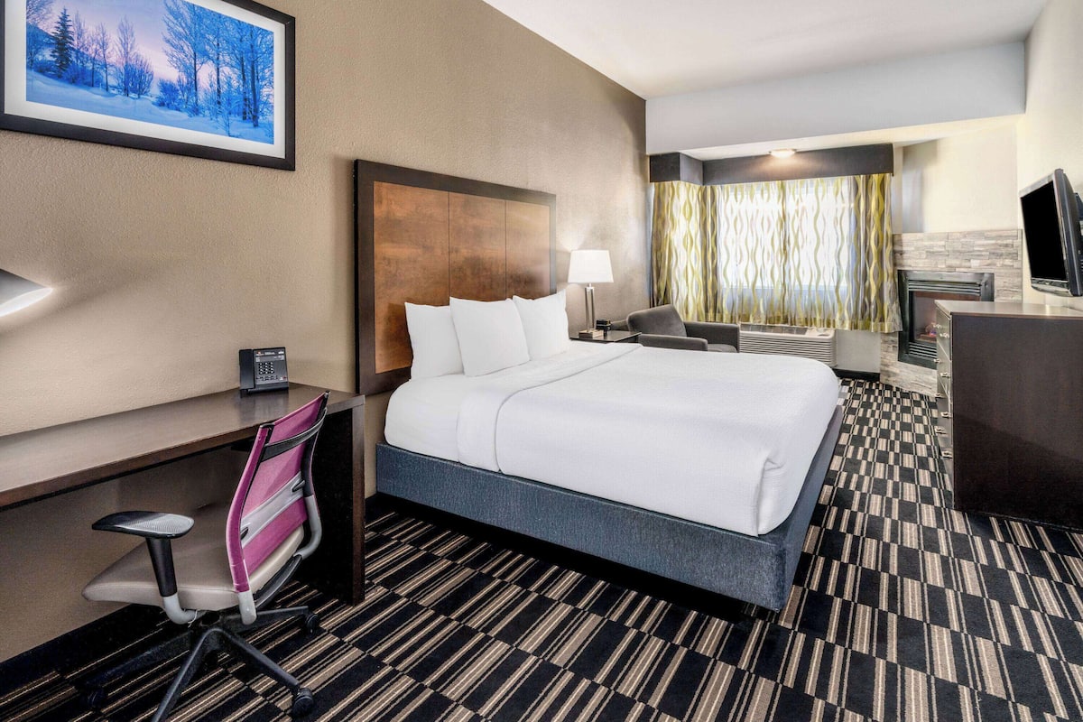 Een hotelkamer met een groot bed, een bureau met stoel, een televisie en een raam met gordijnen.