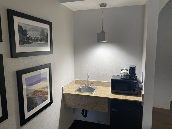 Eine kleine Küchenzeile mit Mikrowelle, Kaffeemaschine und Spüle. An der Wand hängen gerahmte Bilder.
