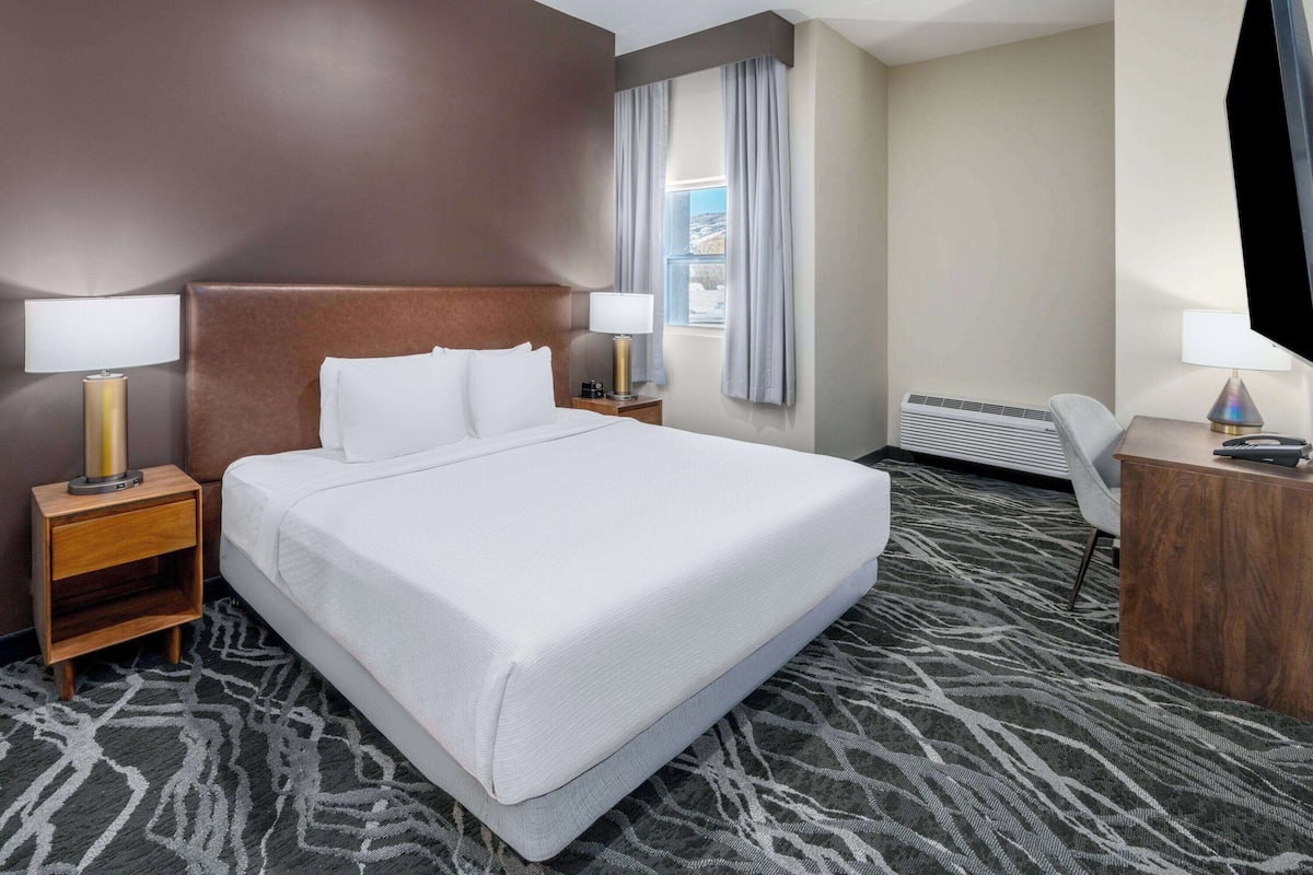 Een hotelkamer met een groot bed, twee nachtkastjes met lampen, een bureau en een stoel.