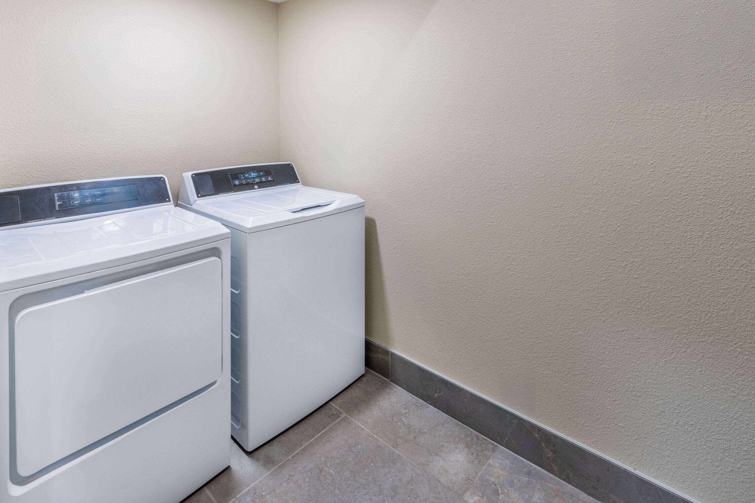 A laundry area with two white front-loading washing machines and a grey tiled floor.