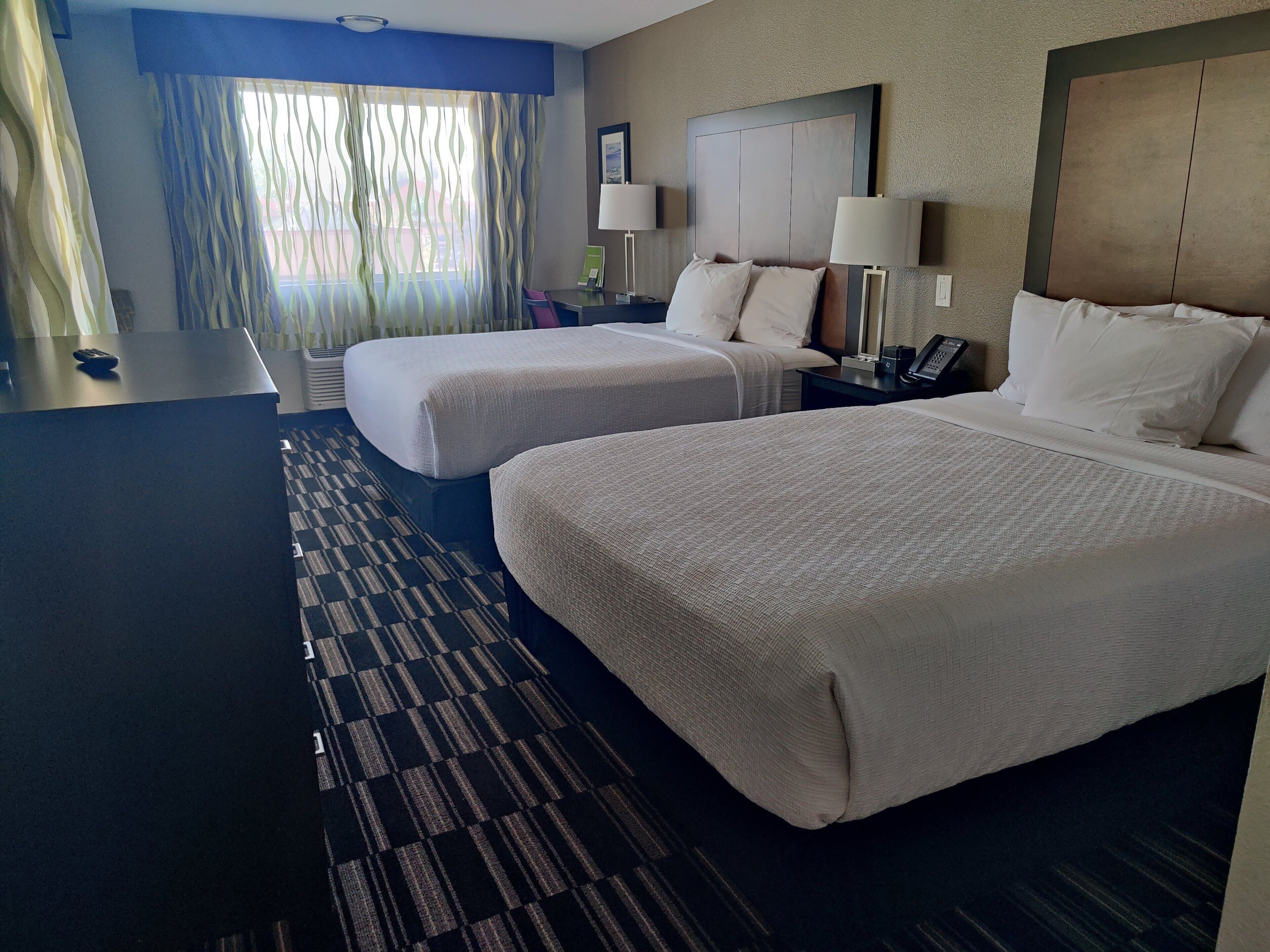 A hotel room with two beds, a desk, and a view of the outdoors.