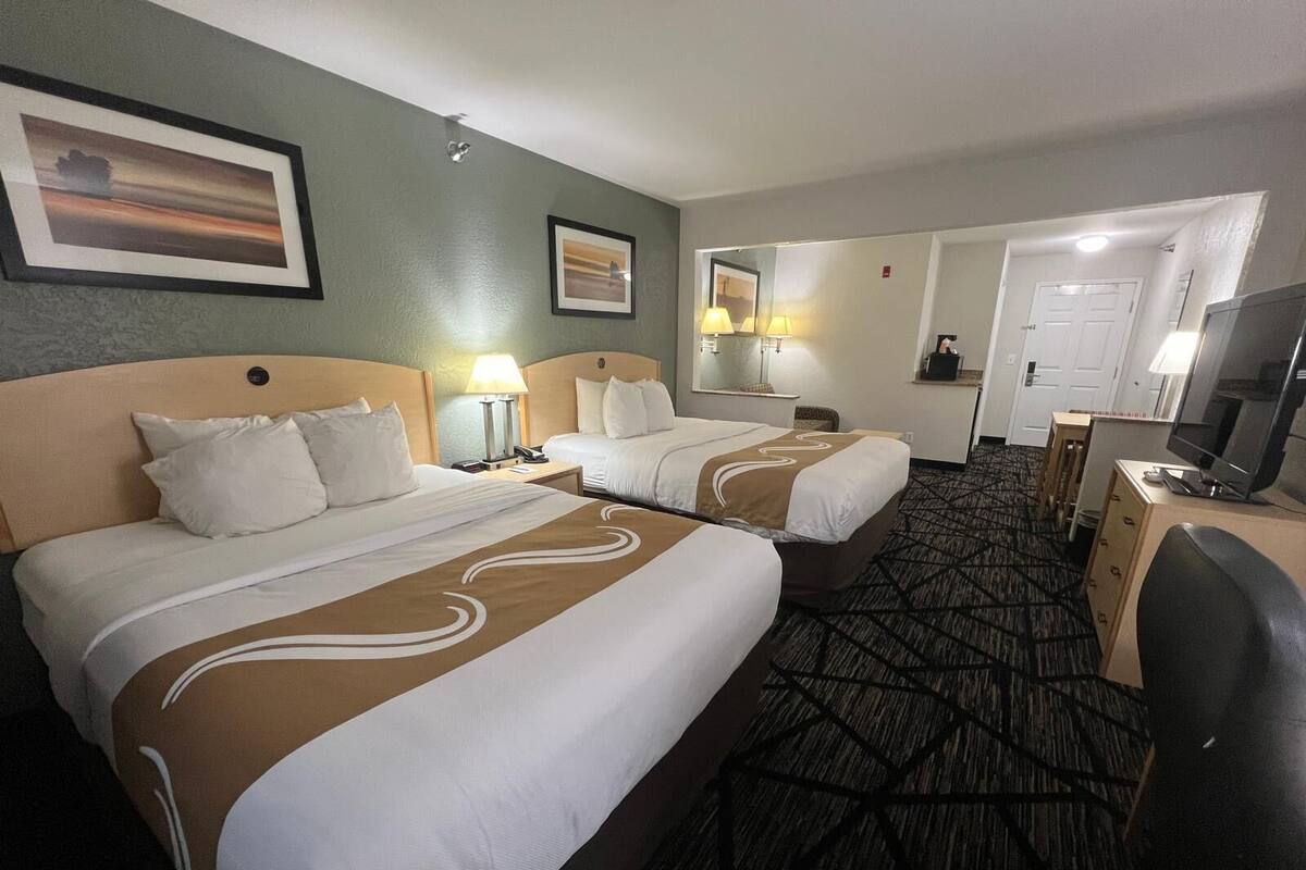 A hotel room with two beds, a desk with a TV, and a bathroom visible through an open door.