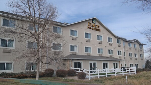 A multi-story hotel with a beige facade, multiple windows, and a white fence with lounge chairs.