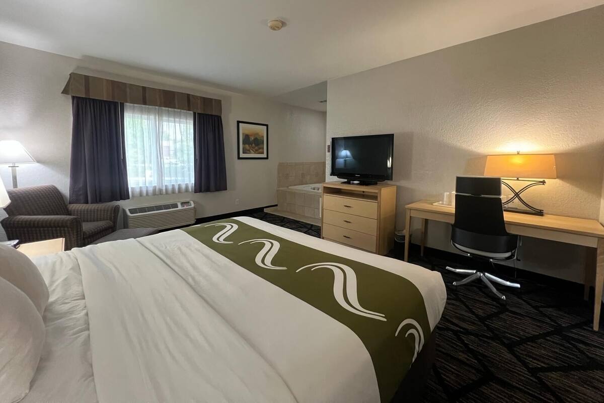 A hotel room with a bed, a desk, a chair, a television, and a window with curtains.
