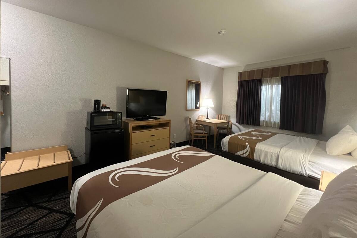 A hotel room with two beds, a desk with a chair, a television, and a microwave.