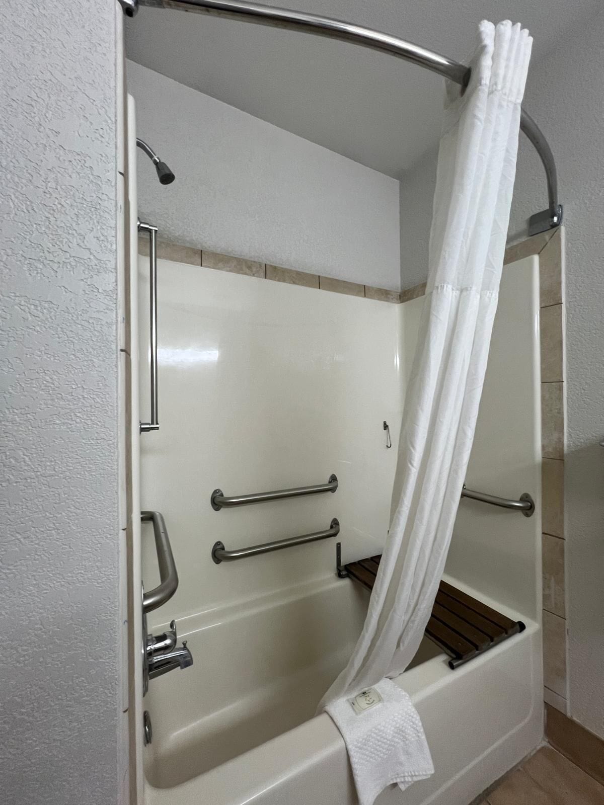 A walk-in shower with a glass door, a white shower curtain, and handrails.
