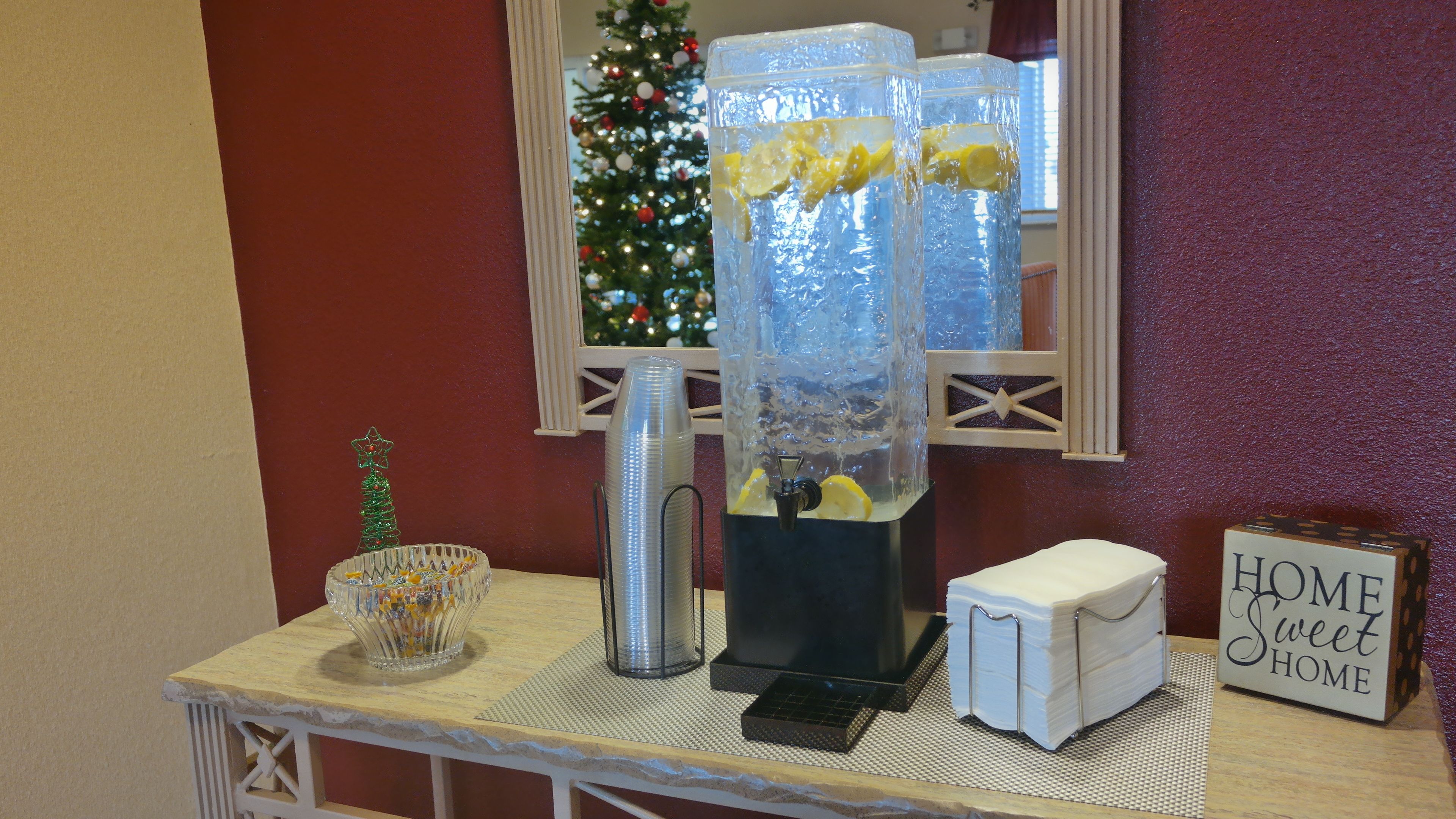 A bathroom counter with a water dispenser, a small decorative tree, and a sign that says "HOME Sweet HOME".