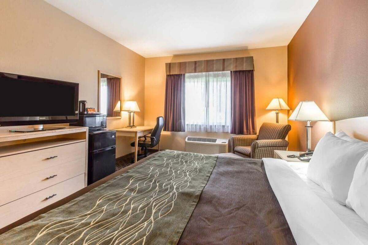 A hotel room with a bed, desk, TV, and a view of the outdoors.