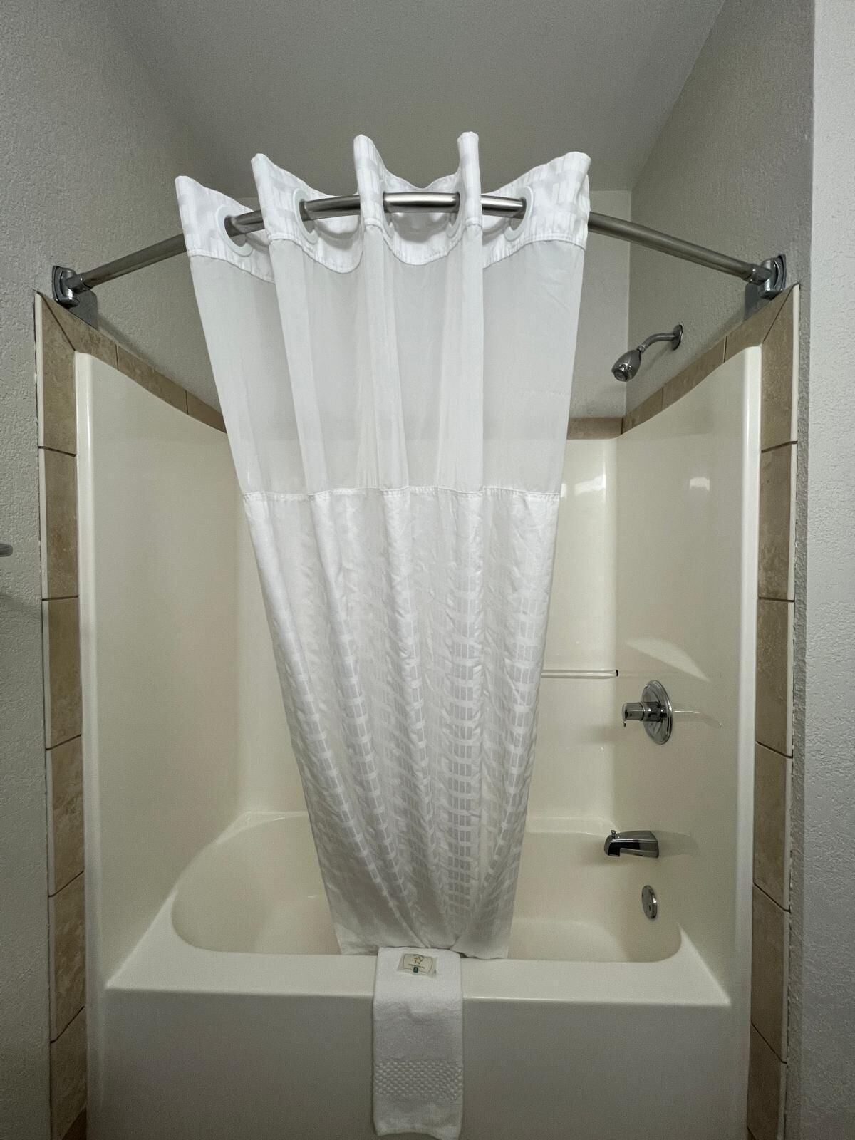 A shower with a white curtain, a handheld showerhead, and a towel rack.