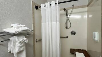A modern bathroom with a glass shower enclosure, a towel rack with folded towels, and a bench with a towel.